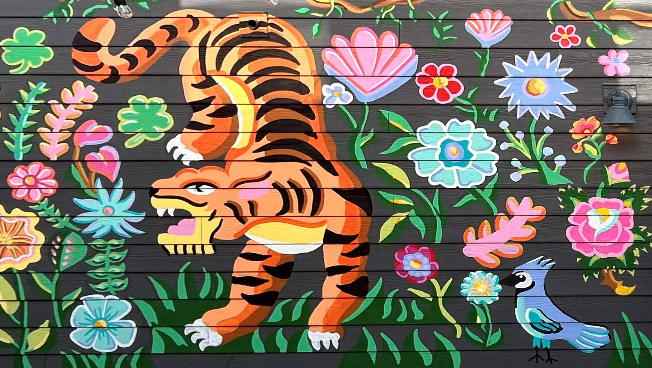 Exterior mural with a tiger and layered botanical shapes across a storefront